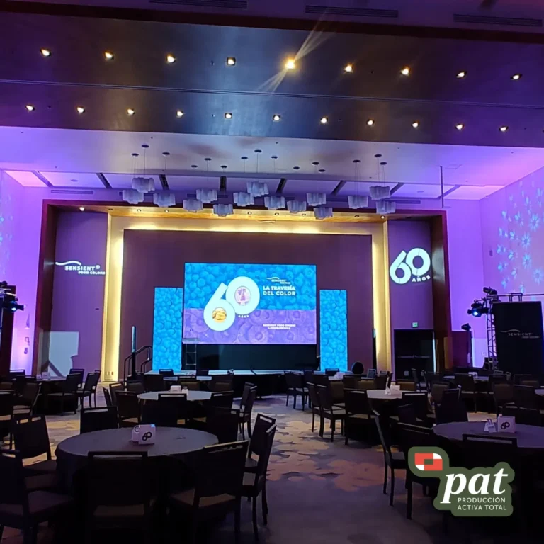 Salón para presentación o conferencia con mesas, sillas, pantalla principal e iluminación profesional.